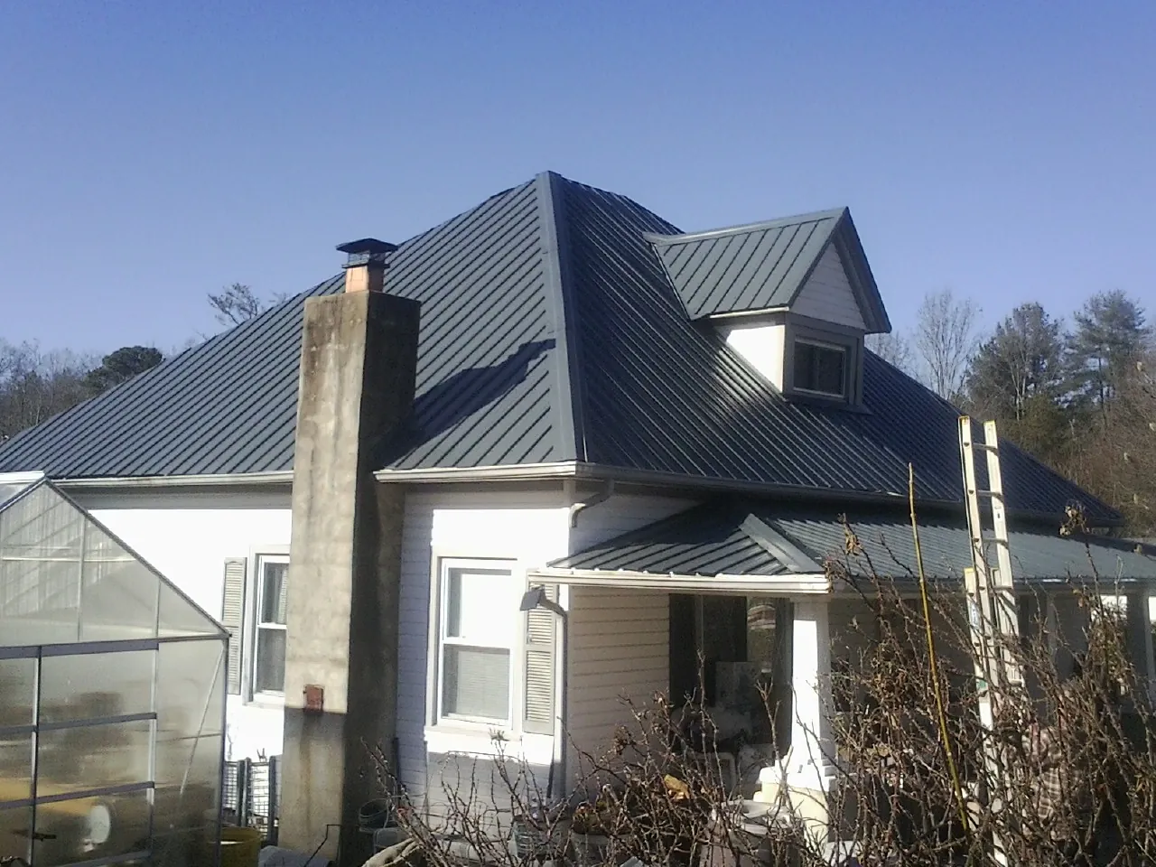 Dark blue standing seam metal roof on a white farmhouse with dormer — Slate & Tile Roof Repair by Roofing Brothers in Sulphur