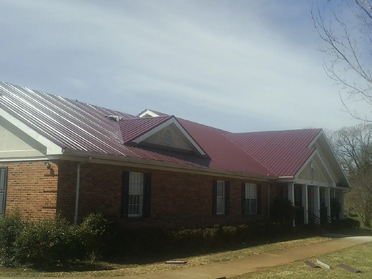 Red metal roof with gabled entries on a long brick building, from a Hail Damage Roof Repair job in Sulphur