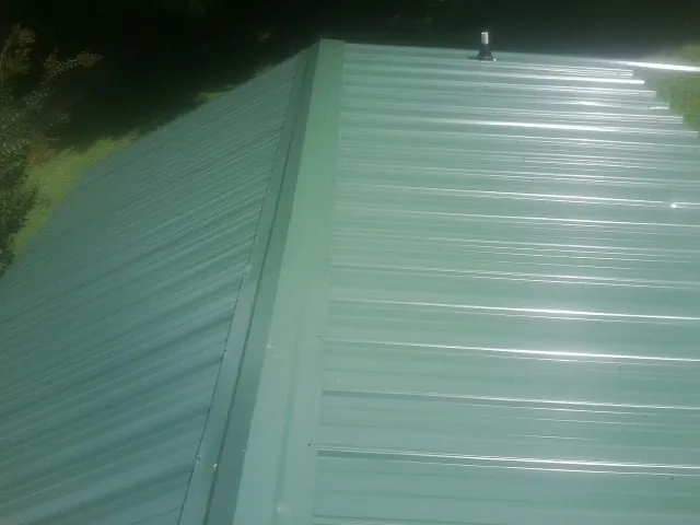 New green metal panels meeting at the ridge of a roof — Flat Roof Repair work by our crew in Sulphur