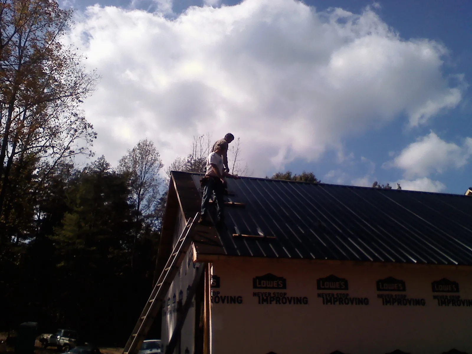 Roofer fastening dark metal panels high against a cloudy sky, from a Roof Inspection job in Sulphur