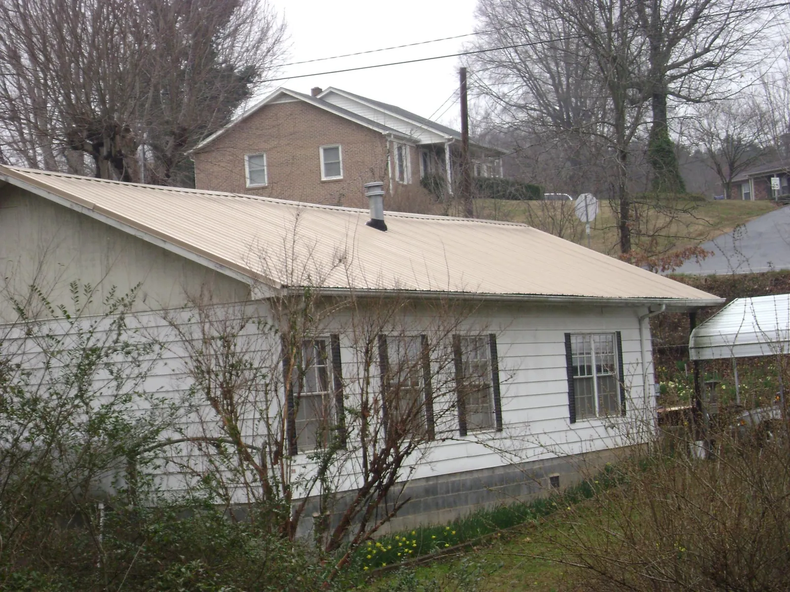 Tan metal roof on a white sided house set into a hillside — Commercial Roofing by Roofing Brothers in Sulphur