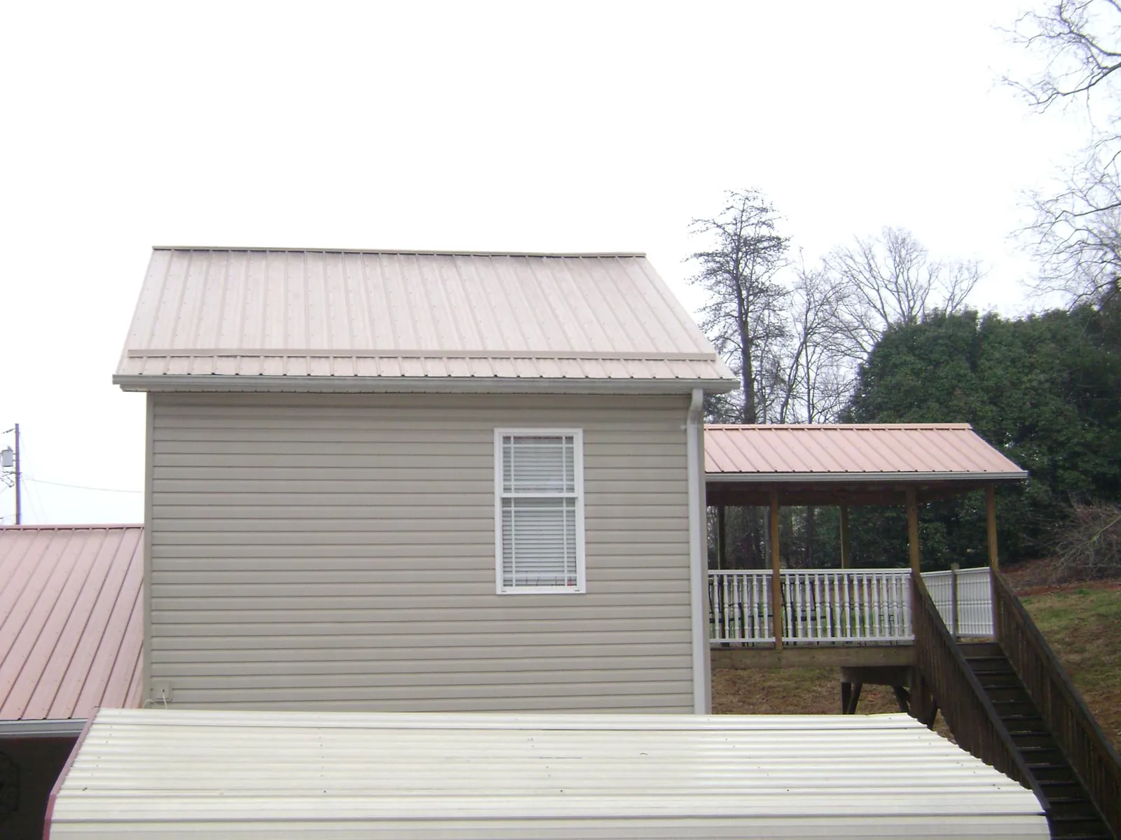 Tan metal roofs on a two story addition and attached porch, from a Roof Replacement job in Sulphur
